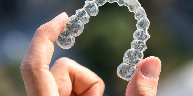 A person holding up an Invisalign clear aligner tray.