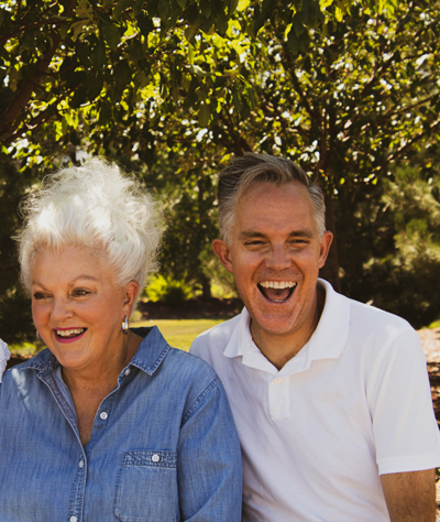 Smiling couple with dental implants in Englewood laughing in the park