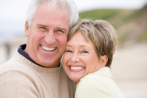 A mature couple embracing on the beach after restorative dental treatments in Englewood.