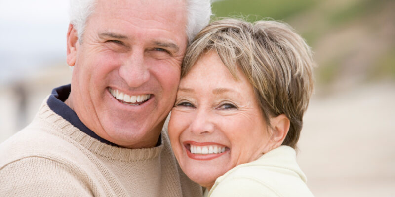 A mature couple embracing on the beach after restorative dental treatments in Englewood.